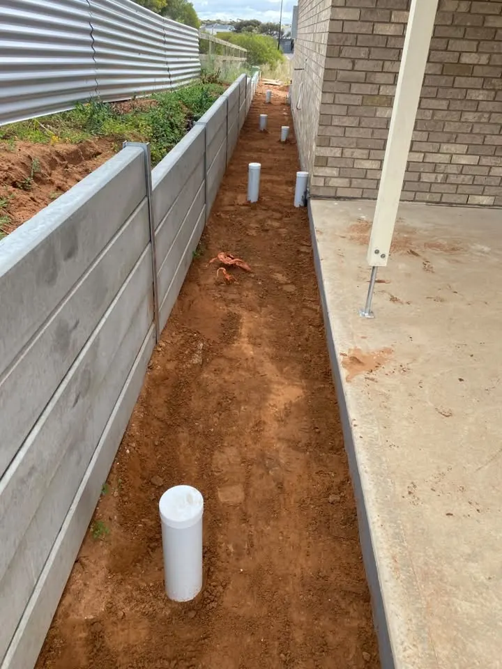 Prepped red dirt beside a retaining wall and a concrete slab