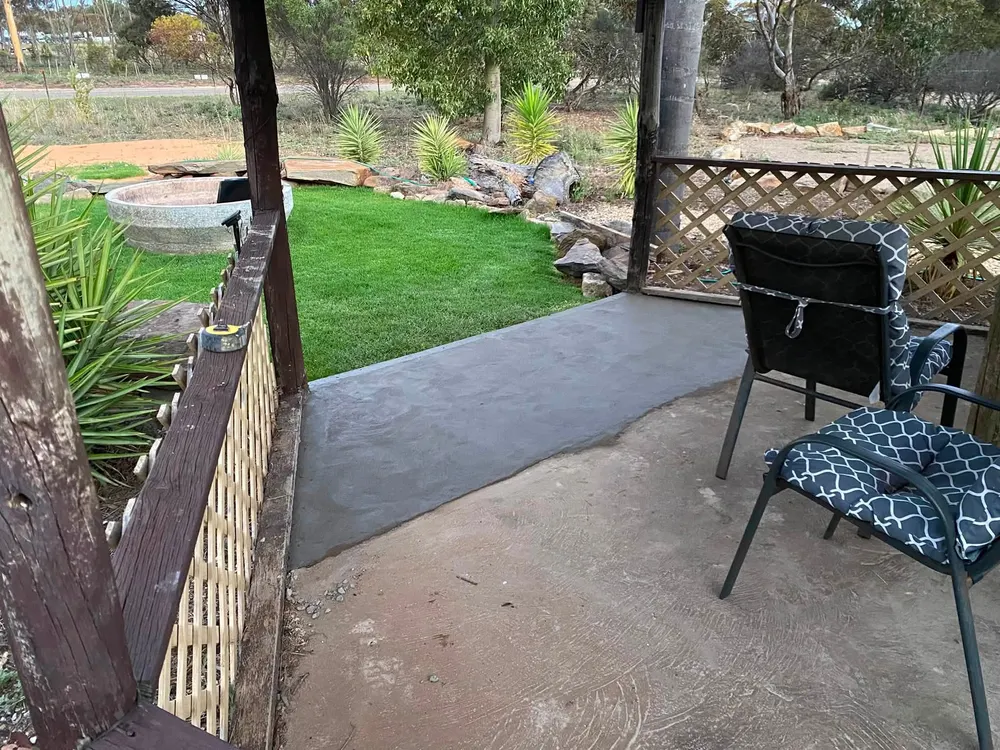 A concrete area with a lawn and garden beyond it